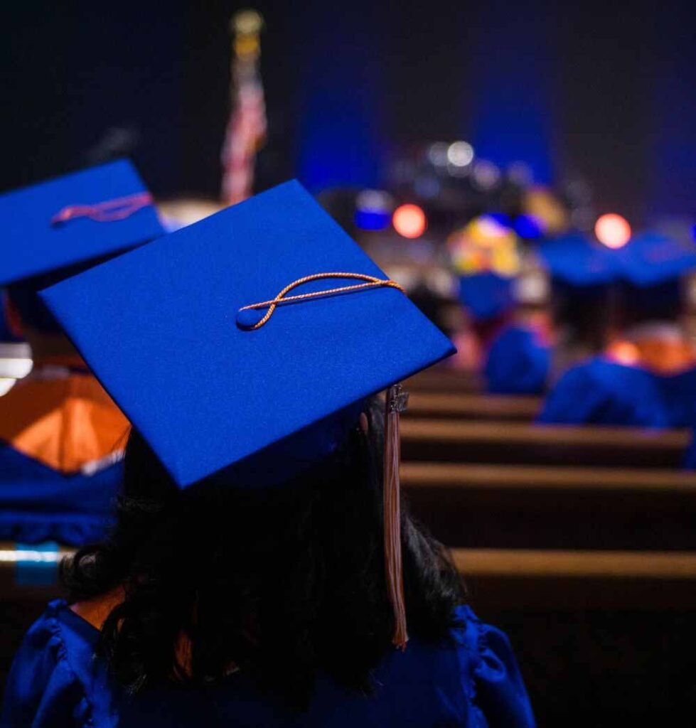 Student sitting at Triumph Public High School graduation ceremony wearing a blue cap and gown.